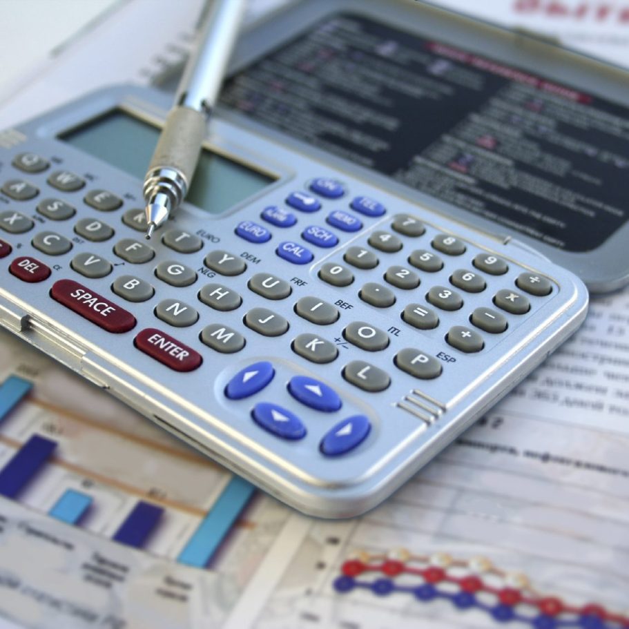 Calculator resting on financial documents with graphs and a pen beside it.